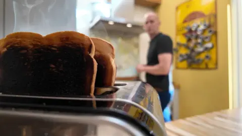Smoke drifts into a kitchen as a man realises he has burned the toast again.