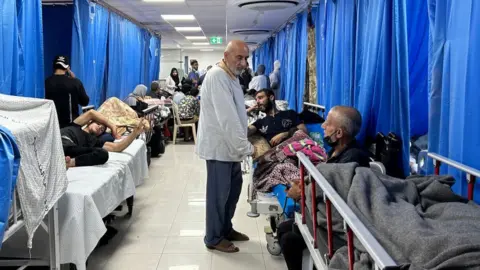 Getty Images A man wanders among hospital patients lying on beds in Gaza's Al-Shifa hospital