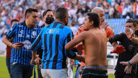 Washington Aguerre of Queretaro attempts to calm fans who reached the pitch