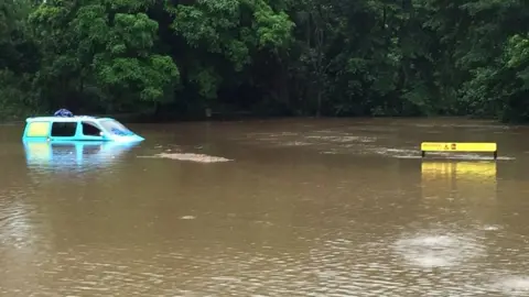 PA A campervan half-submerged in a river near a sign warning of crocodiles