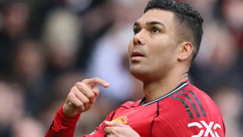 Manchester United midfielder Casemiro points to the club badge on his red shirt 