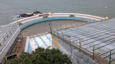 Tinside Lido. Scaffolding covers a building. Seawater surrounds the outside of the lido.