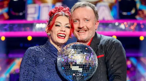 Diane and Chris lift up the glitterball trophy together smiling at the camera