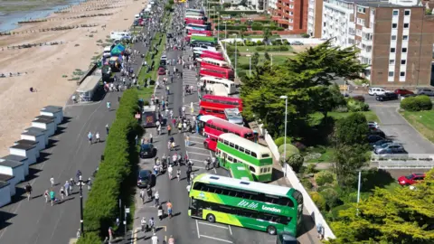 Aerial shot of Worthing Bus Rally 2024 showing buses of various ages parked up on the seafront with crowds looking at them 