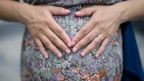 Getty Images Expectant mother Jamie Chui, 33, rests her hands upon her baby bump, while living in lockdown in Hong Kong