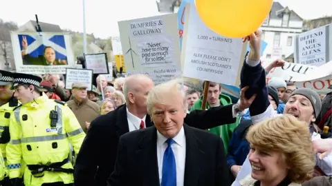 Getty Images A protester rubs Donald Trump's hair with a balloon, making it stand up