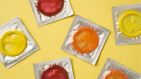 Getty Images Stock image of condoms - six coloured condoms that are yellow, red and orange wrapped in silver foil are placed against a pale yellow background