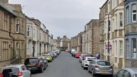 Google General street view of  Kensington Road in Morecambe, showing terraced houses on each side with bay windows, most of which have cars parked outside