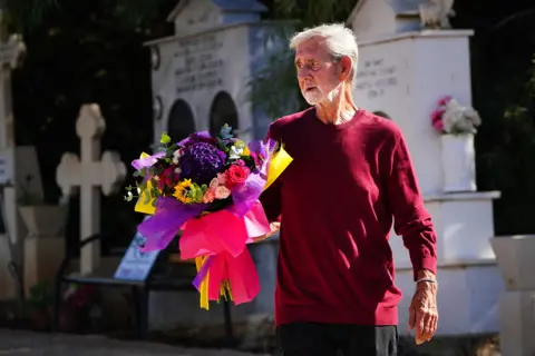 Victoria Jones/PA David Hunter lays flowers at the grave of his wife Janice Hunter at a cemetery near their their former home in Paphos, Cyprus. August 1, 2023.