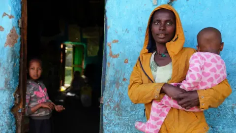 Getty Images A woman and her children look on as food aid and mattresses are delivered to the Day Care centre turned IDP camp they currently reside in on October 11, 2021