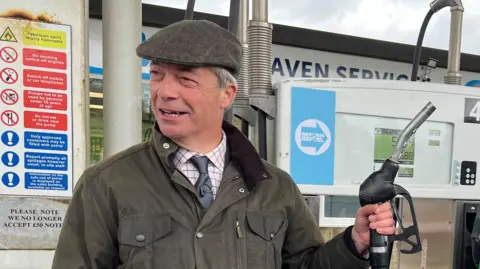 Nigel Farage holds at a petrol station filling up a car