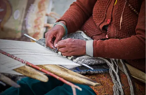 Andrew Newey A woman weaves threads on a loom on her lap