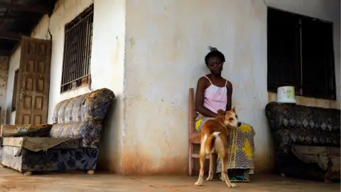 Reuters A woman sits with her dog outside her house on the outskirts of Yaounde, Cameroon, 9 October 2018.