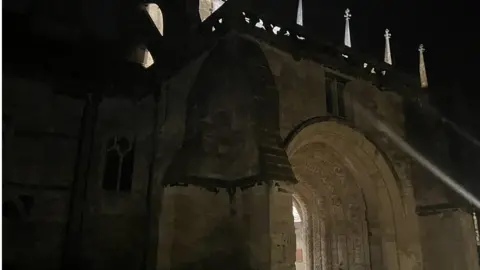 BBC Malmesbury Abbey's porchway, a large archways with carvings, at night with a light shining from inside