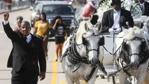 Getty Images A man holds his hand up in solidarity as the remains of George Floyd are brought by horse-drawn carriage in a funeral procession to Houston Memorial Gardens Cemetery for burial on June 9, 2020 in Pearland, Texas
