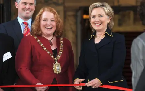 Pacemaker Hillary Clinton, standing alongside Naomi Long cuts a red ribbon to reopen the refurbished Belfast City Hall