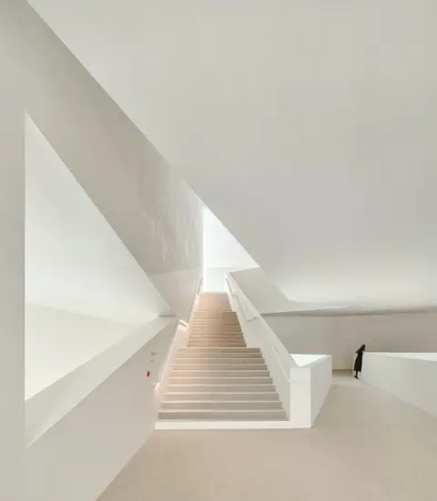 Eugeni Pons / APA18 View of bright walls and a staircase with a solitary figure in black