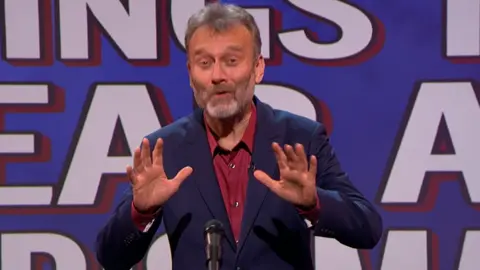 Hugh Dennis standing in front of a microphone