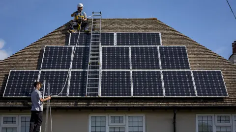 Getty Images Solar roof fitters construct an array of panels