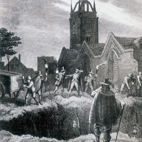 Getty Images An engraving showing men digging a large plague pit at night beside a church, lowering bodies into a mass grave by torchlight.
