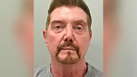 Custody image of Stephen Tate with ginger hair and beard wearing a grey top.