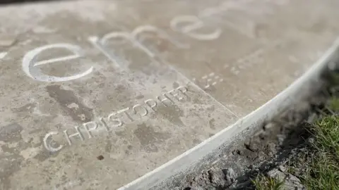 The name Christopher Garrett engraved on the round base of the light coloured stone war memorial.