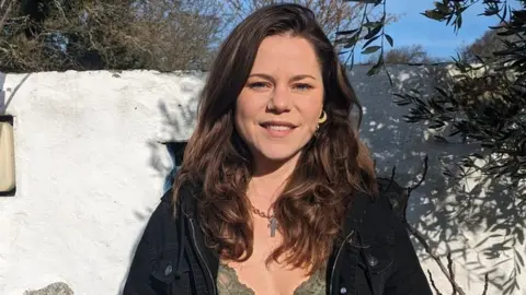 Florence Pardoe Ms Pardoe smiling whilst standing next to a white wall outside on a sunny day