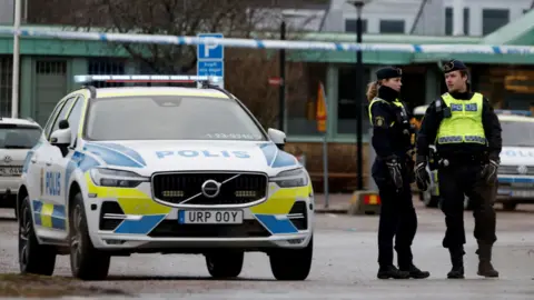 Swedish police officers stand next to a police car