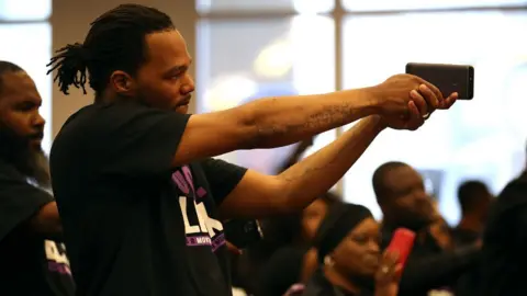 Getty Images An attendee of the special council meeting holds a phone like a gun