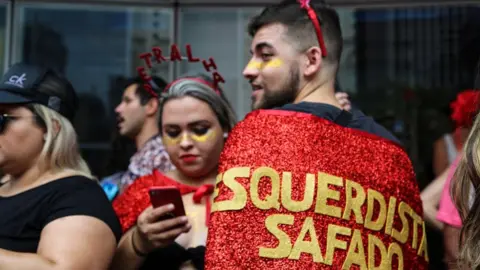 BBC A man wears a cape emblazoned with the phrase "shameless left"