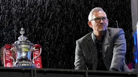 PA Media Gary Lineker in a rainy stadium by the FA Cup trophy