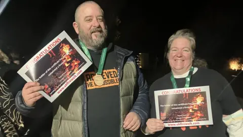 Children’s Hospice South West A man and a woman holding certificates showing their completion of the fire walk