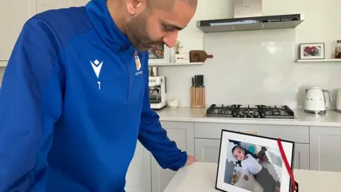 Man in blue football top looking over a picture of baby in a frame
