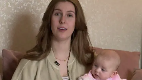 Rachel Hargreaves sits on a sofa with her baby daughter Joni in her arms