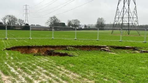 Supplied Sink hole in a field by an electricity pylon