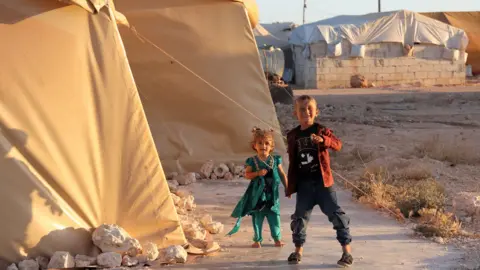 Children walk outside a tent at the "Blue Camp" for Syrians displaced by conflict near the town of Maaret Misrin in rebel-held Idlib province (10 July 2022) during the Muslim holiday of Eid al-Adha on July 10, 2022