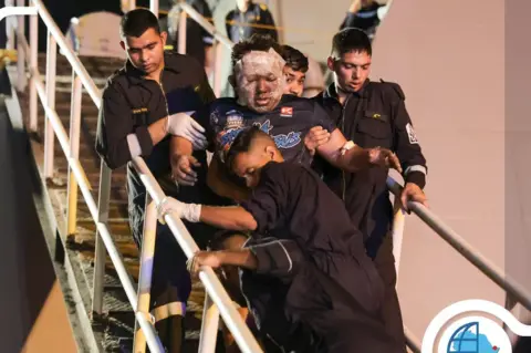 Djibouti Ports Authority Handout photo posted on X by the Djibouti Ports Authority showing an injured member of the True Confidence's crew being helped off an Indian Navy warship in Djibouti (6 March 2023)