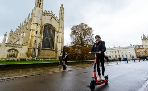 Voi Woman riding past King's College Chapel in Cambridge on e-scooter