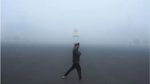 Getty Images A man walking in Delhi as heavy smog shrouds buildings in the city