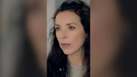 A woman looks annoyed. She has long brown hair.