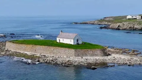 A small white church is seen standing on an island