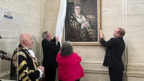 Councillor Jacqui Rayment, with the current Lord Mayor Dave Shields, and they are looking at the portrait of Jacqui which is being unveiled by two men.