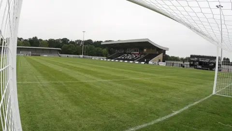 Getty Images A wide angle view of Corby Town's Steel Park stadium from inside the corner of one of the goals. The green pitch is framed by a small all-seated stand with a curved roof and a terraced end behind the opposite goal.