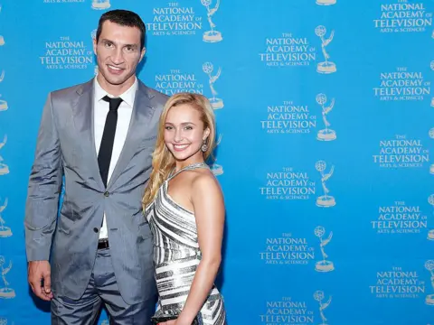 Getty Images Wladimir Klitschko in a grey suit, white shirt and black tie is pictured smiling with his arm around Panettiere, who is smiling and has long blonde hair and wears a silver and white halterneck dress at an Emmy Awards reception in 2013. 