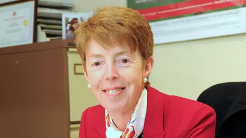 PA Former Post Office boss Paula Vennells sits in an office at a desk smiling at the camera