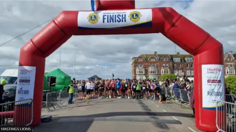 Lions Club of Hastings A group of runners crossing a finishing line at a half marathon event.