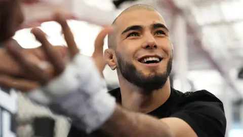 Getty Images Muhammad Mokaev, a man, is smiling as he has his hands wrapped with white bandages prior to his fight