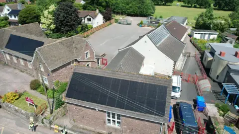 Aerial view of school with solar panels on two buildings and cars parked nearby.