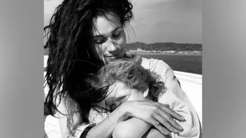 Meghan hugs Lilibet near open water