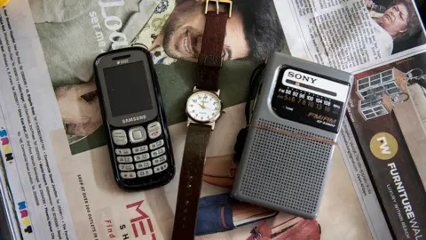 Sayan Hazra A mobile phone, a watch and a radio transmitter lying on a newspaper in a room at the care home